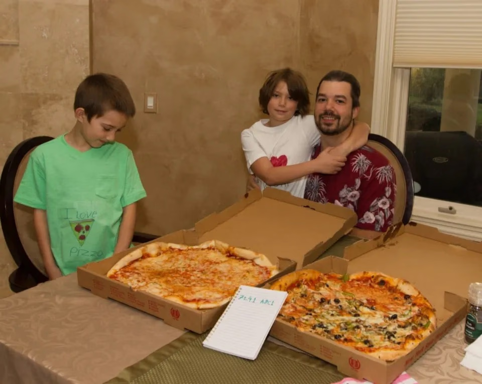 A photo of people gathered around a table sharing two pizzas.