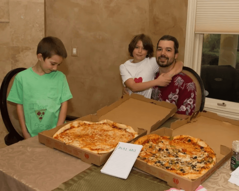 Ein Foto von Leuten, die sich um einen Tisch versammelt haben und zwei Pizzen teilen.